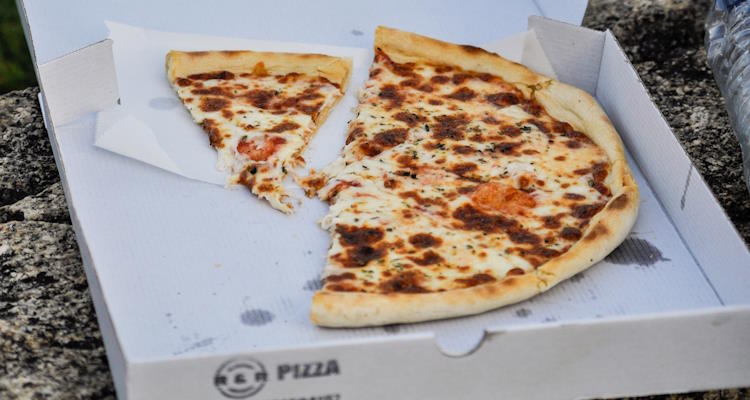 Geöffneter Pizzakarton mit einem angeschnittenen Stück Pizza. Backpapier, Bratpfanne oder Pizzakartons - diese und viele andere Produkte können PFAS enthalten.