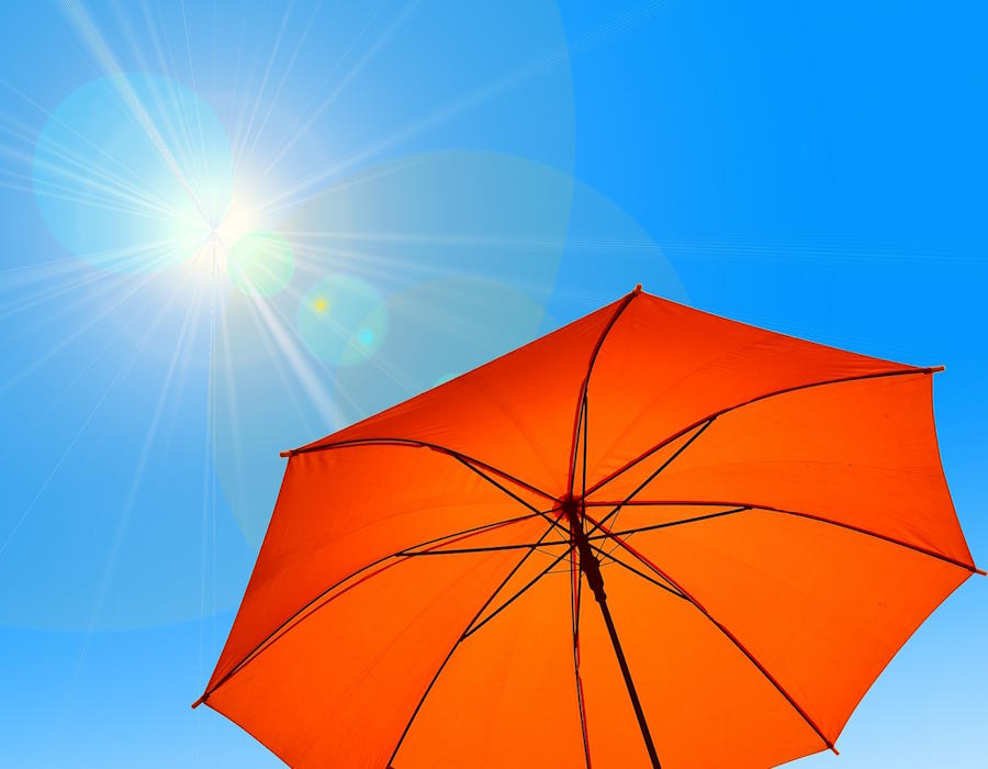 Geöffneter orangefarbiger Regenschirm. Im Hintergrund blauher Himmel mit strahlender Sonne Geöffneter orangefarbiger Regenschirm. Im Hintergrund blauher Himmel mit strahlender Sonne