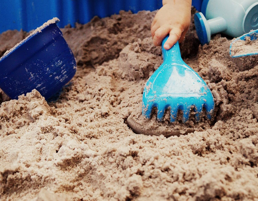 Sankasten mit Sandspielzeug. Eine Kinderhand benutzt eine hellblaue Spielharke. Sankasten mit Sandspielzeug. Eine Kinderhand benutzt eine hellblaue Spielharke.
