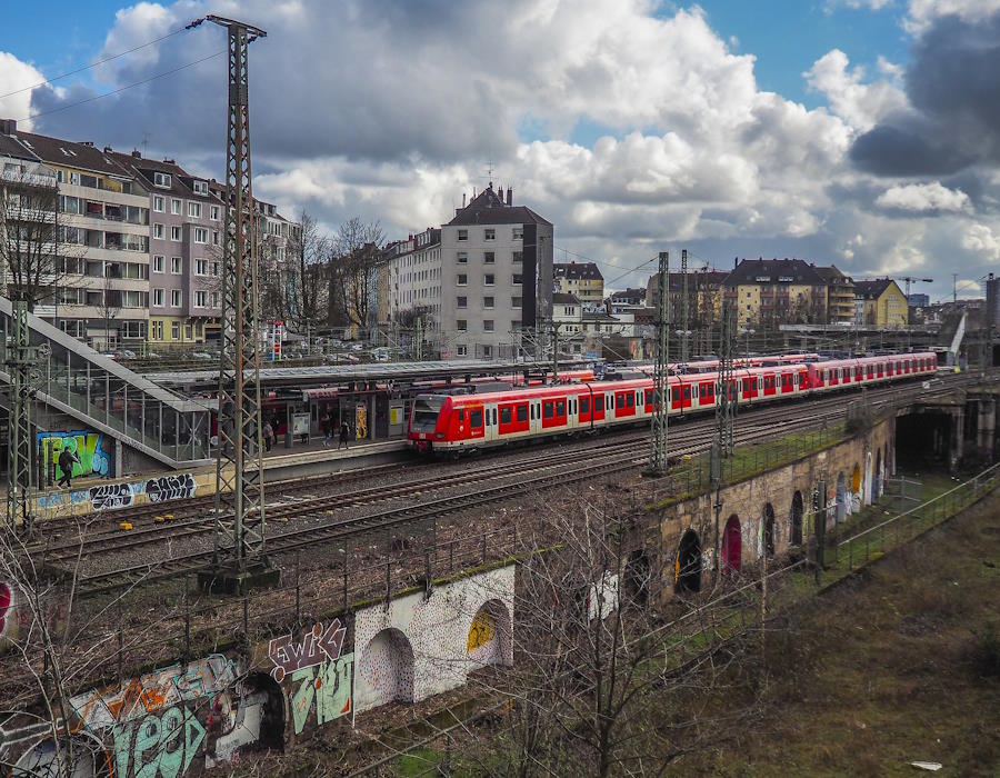Im Hintergrund Wohngebäude. Im Vordergrund ein S-Bahnhof mit einfahrendem Zug. Im Hintergrund Wohngebäude. Im Vordergrund ein S-Bahnhof mit einfahrendem Zug.