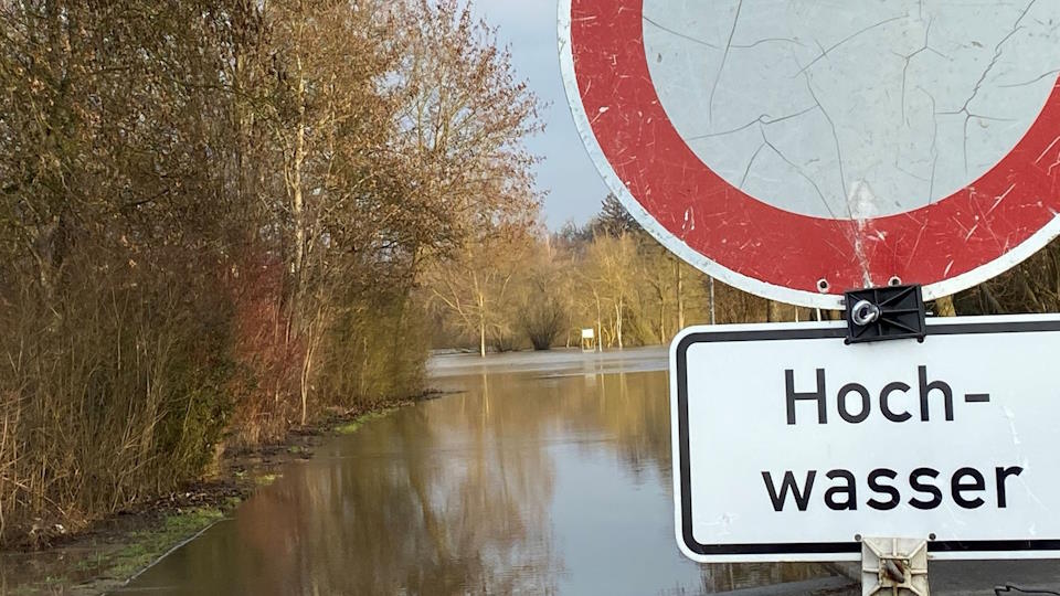 Warnschild Hochwasser. Im Hintergrund befinden sich überflutete Flächen 