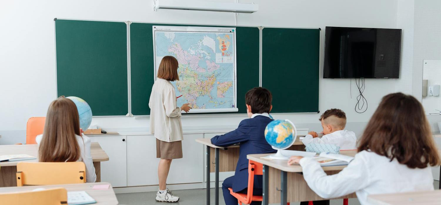 Symbolbild: Eine Schulklasse sitz in einem Klassenraum ohne Fenster. Eine Lehrerin steht vor der Klasse und unterrichtet. Es gibt keine Fenster in dem Klassenraum. Symbolbild: Eine Schulklasse sitz in einem Klassenraum ohne Fenster. Eine Lehrerin steht vor der Klasse und unterrichtet. Es gibt keine Fenster in dem Klassenraum.