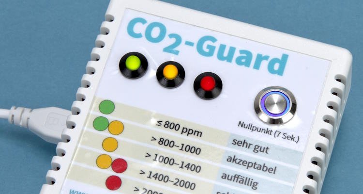 Symbolbild: Weißes, viereckiges Kohlendioxid-Messgerät aus Kunststoff mit leuchtender LED-Anzeige. Eine CO2-Ampel zeigt an, wann gelüftet werden muss. Dann leuchtet das Lämpchen gelb oder sogar rot.