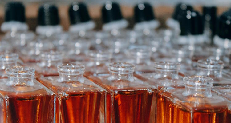 Symbolbild: Viele aufgereiht Parfumflakons aus Glas mit einer farbigen Flüssigkeit. Duftstoffe können die Innenraumluft belasten.