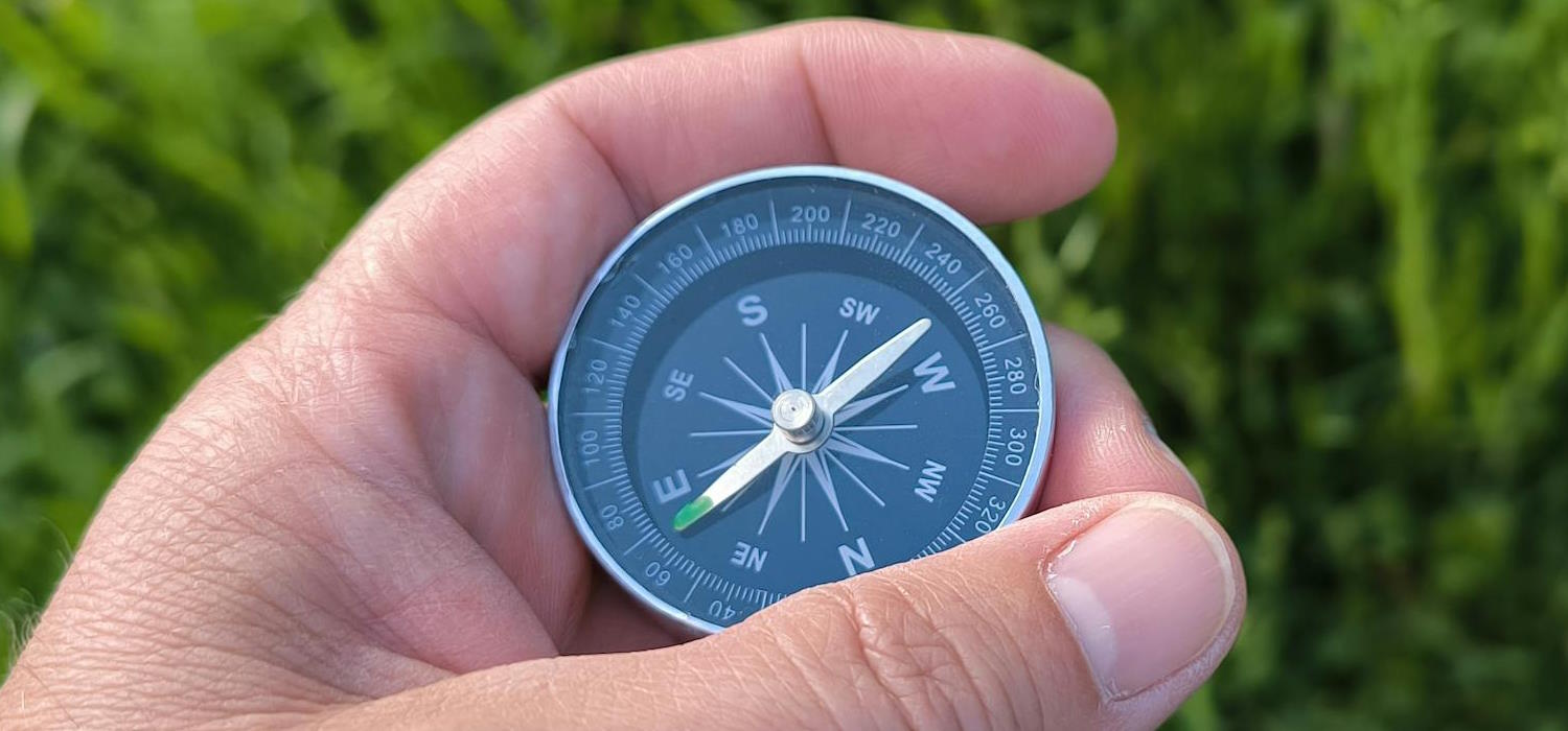Symbolbild: Eine Hand hält einen Kompass. Im hintergrund ist unscharf der mit Gras bewachsene Boden zu erkennen. Symbolbild: Eine Hand hält einen Kompass. Im hintergrund ist unscharf der mit Gras bewachsene Boden zu erkennen.