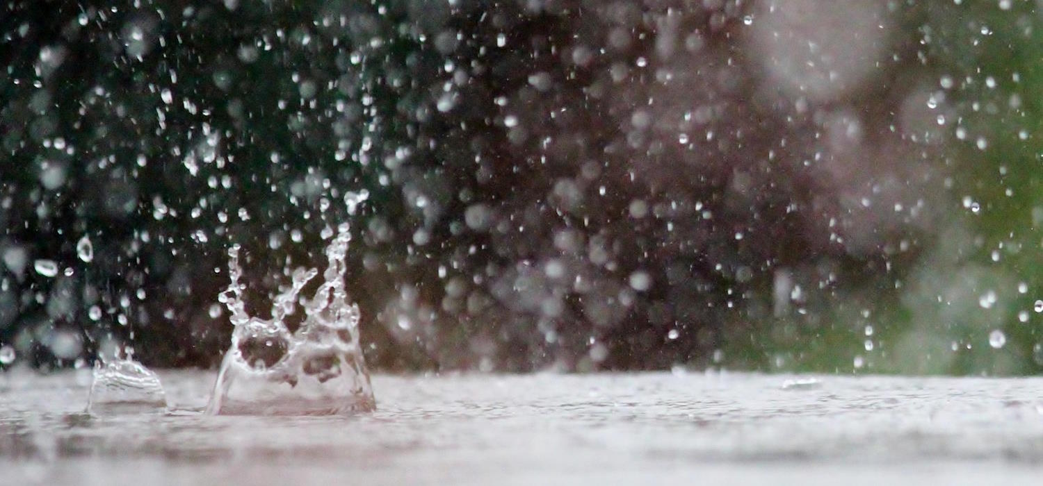 Regentropfen fallen in eine Pfütze und lassen das Wasser wieder hochspritzen.