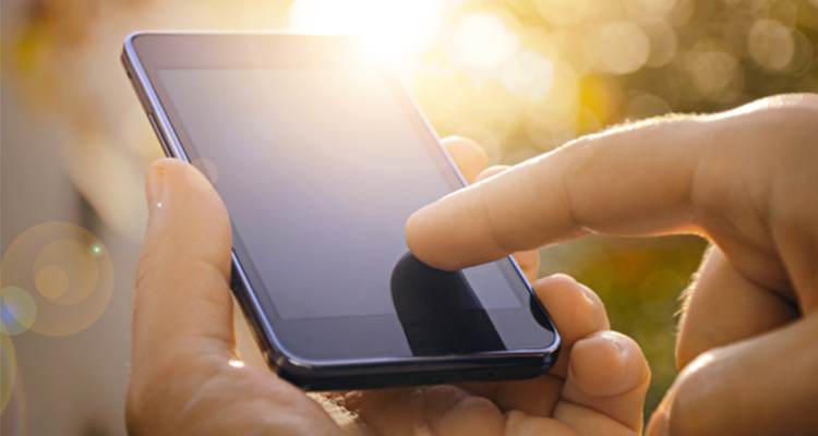 Hand, die ein Smartphone im Sonnenlicht bedient.