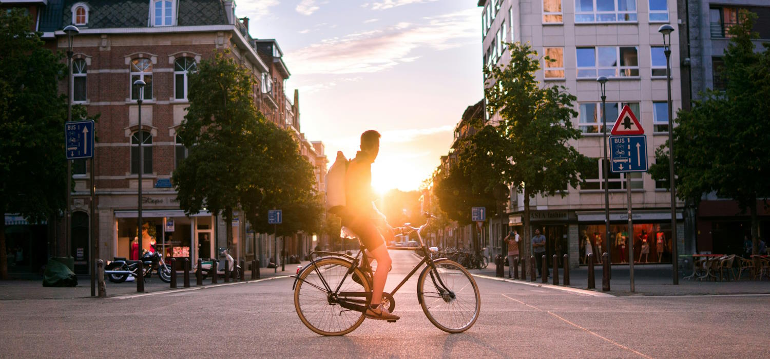 Das Bild zeigt einen Fahrradfahrer auf einer Kreuzung in einer Stadtlandschaft bei Sonnenuntergang Das Bild zeigt einen Fahrradfahrer auf einer Kreuzung in einer Stadtlandschaft bei Sonnenuntergang