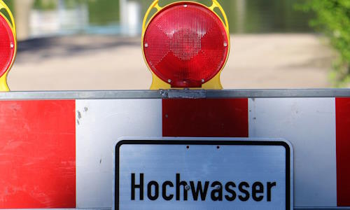 Gesperrte Straße mit Hinweisschild. Im Hintergrund durch Hochwasser überschwemmter Bereich