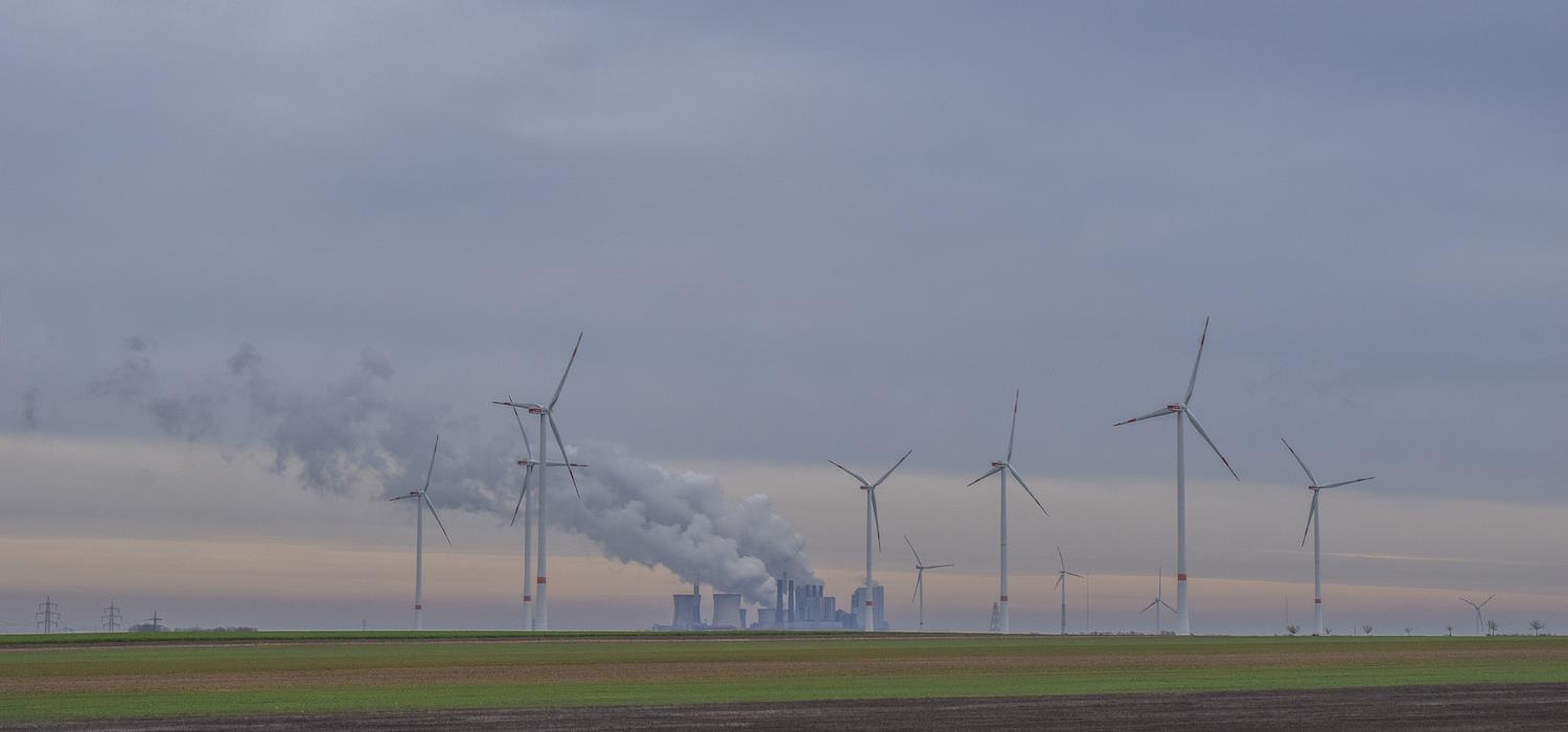 Windenergieanlagen mit einem Kraftwerk und rauchenden Schornsteinen im HIntergrund Windenergieanlagen mit einem Kraftwerk und rauchenden Schornsteinen im HIntergrund