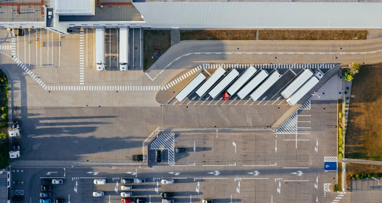 Symbolbild: Luftaufnahme eines Speditionsgeländes, ein großer asphaltierter Parplatz mit parkenden LKW.