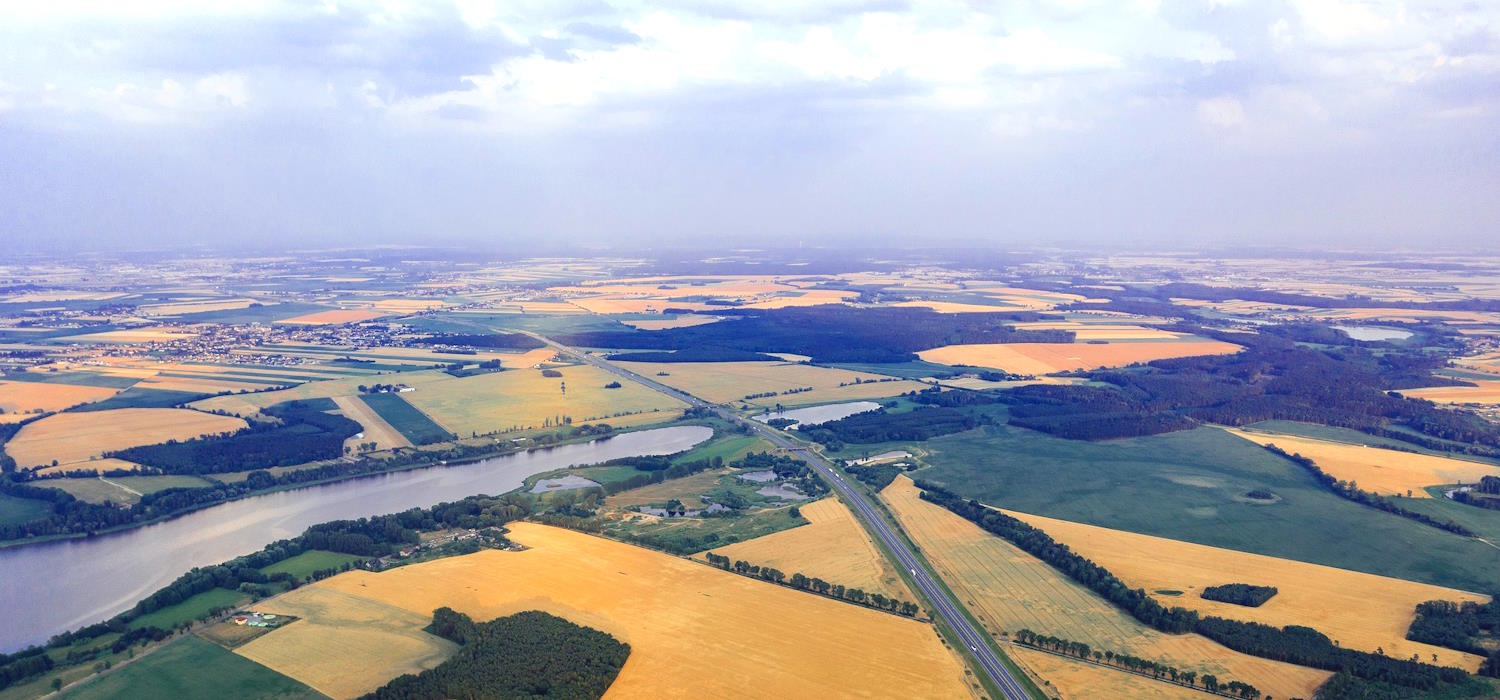 Symbolbild: Luftbildaufnahme von bewirtschafteten Ackerflächen. Durch die Bildmitte verläuft ein Fluss. Eine Straße überquert den Fluss über eine Brücke. Symbolbild: Luftbildaufnahme von bewirtschafteten Ackerflächen. Durch die Bildmitte verläuft ein Fluss. Eine Straße überquert den Fluss über eine Brücke.